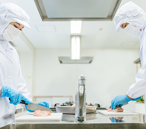 衛生服と手袋を着用した作業員が厨房で食肉を加工している様子